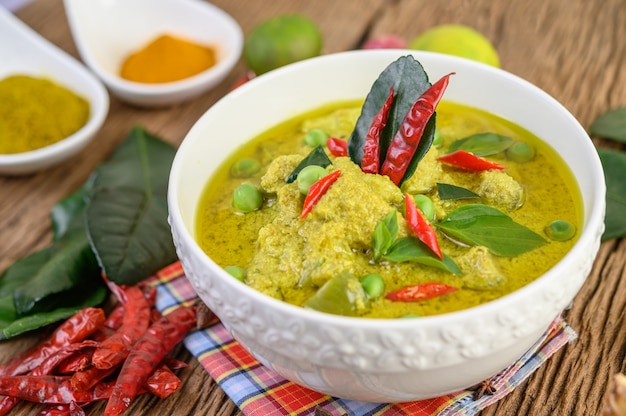 Gratis foto groene curry in een kom en kruiden op houten tafel.