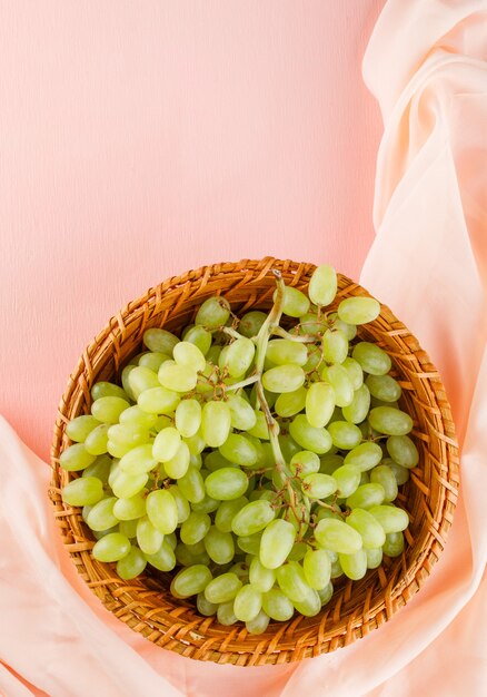 Groene druiven in een rieten mand op roze en textiel.