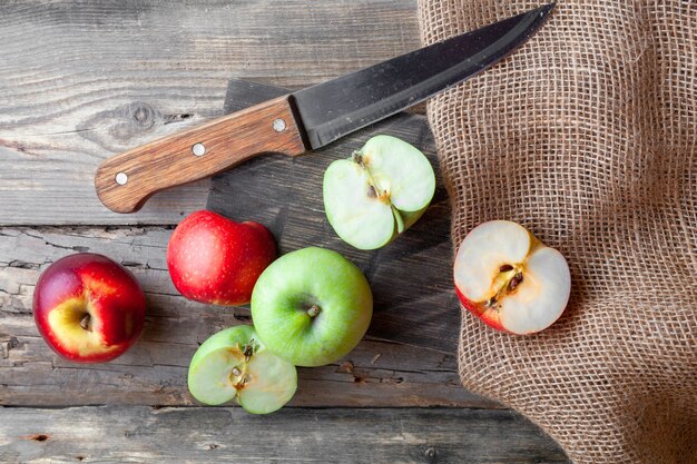 Groene en rode appels in de helft gesneden met mes, hout en doek bovenaanzicht op een donkere houten achtergrond