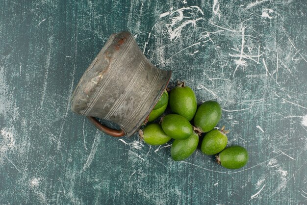 Groene feijoa-vruchten die uit de vaas op marmeren oppervlakte vallen.