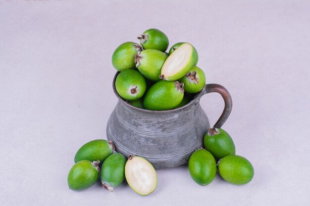 Groene feijoas in een metalen pot op een grijze ondergrond