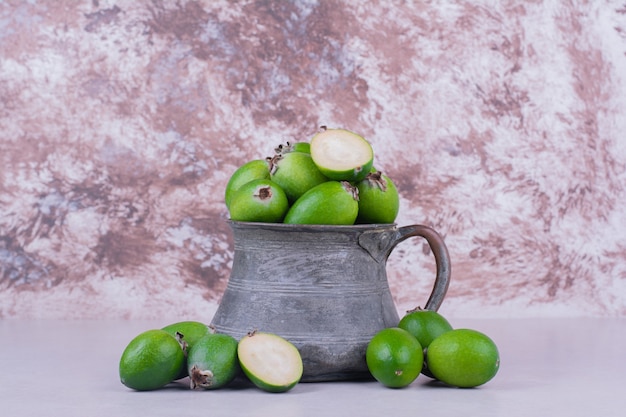 Groene feijoas in een metalen pot op grijs.