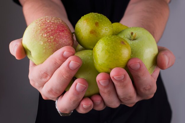 Groene kersenpruimen en appels in de handen van een persoon