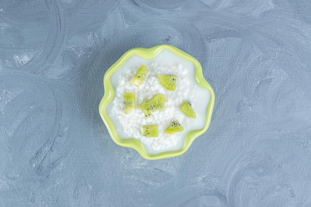 Gratis foto groene kom gevuld met rijstpudding en gegarneerd met stukjes kiwi op marmeren tafel.