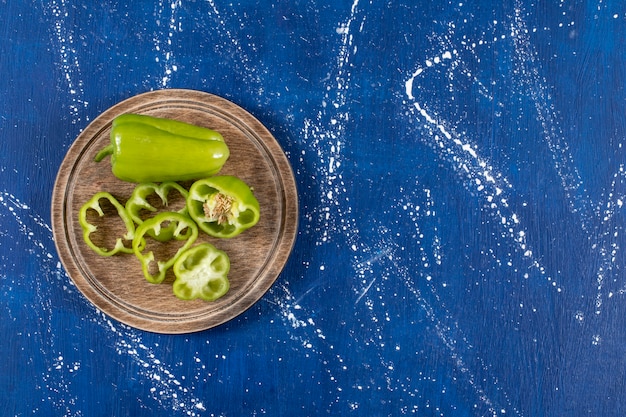 Groene paprika en plakjes op een houten bord op marmeren oppervlak