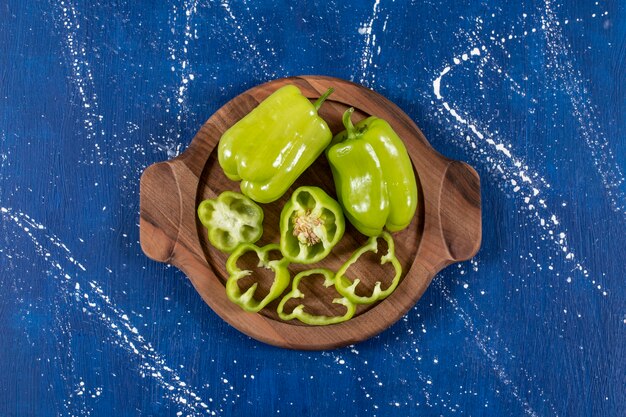 Groene paprika's en ringen op een houten bord op marmeren oppervlak