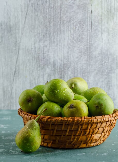 Groene peren in een mand op gips en grungy muur. zijaanzicht.