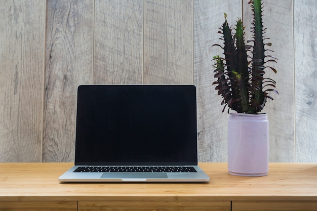 Groene plant in kan met een open laptop op houten bureau