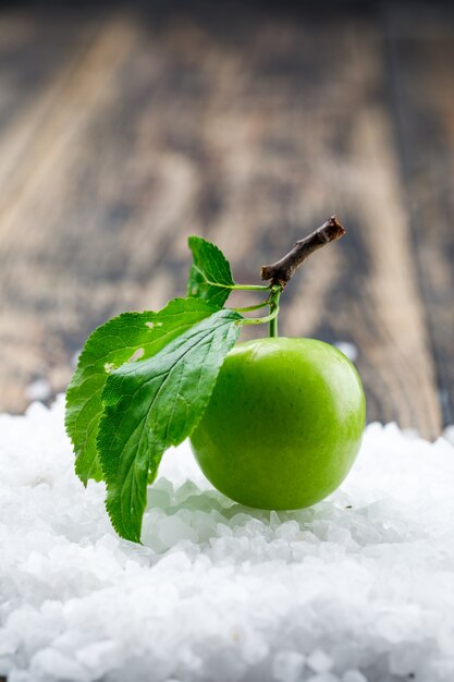 Groene pruim met bladeren en zoutkristallen op houten muur, zijaanzicht.