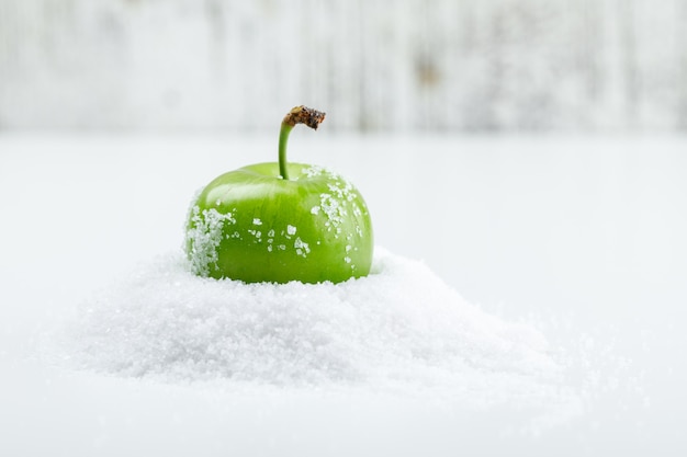 Groene pruim met zoutkristallen op witte en grungy muur, zijaanzicht.