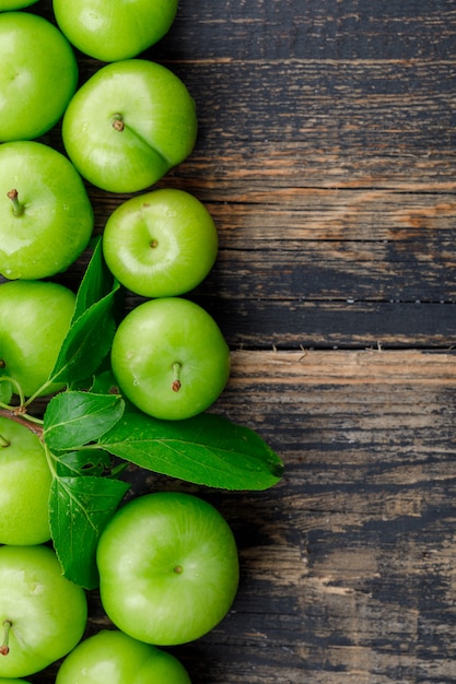 Groene pruimen met bladeren op houten muur, plat lag.