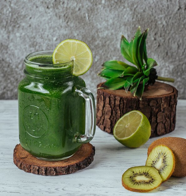 Groene smoothie in metselaarpot met limoenplak, gegarneerd met plakjes kiwi