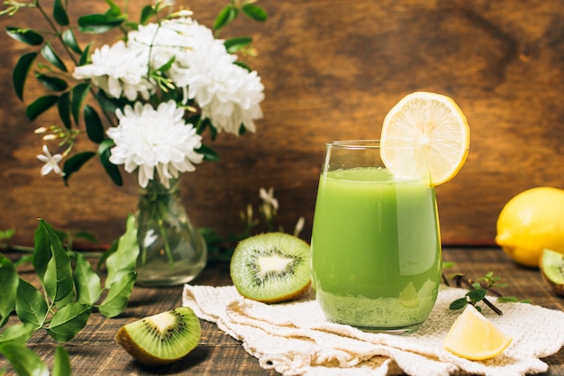 Gratis foto groene smoothie naast vaas met bloemen