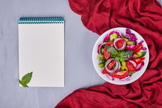 Groentesalade met gesneden en gehakte voedingsmiddelen in een witte plaat met een receptenboek opzij.