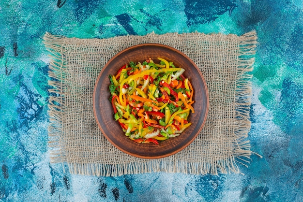 Groentesalade op een plaat op de jute, op de blauwe achtergrond.