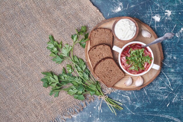 Groentesoep in een witte kop met donker brood op een houten bord.