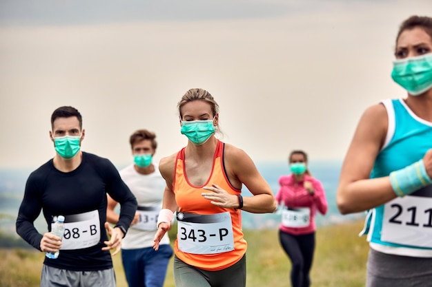 Groep atletische mensen die beschermende gezichtsmaskers dragen tijdens het lopen van een marathon tijdens virusepidemie Focus ligt op vrouw in oranje shirt