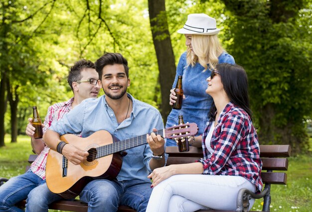 Groep blanke vrienden, gitaar spelen, bier drinken en rondhangen op een bankje in het park