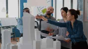 Gratis foto groep collega's die samenkomen om het bouwmodel en maquette te analyseren om blauwdrukken te plannen. mensen die werken aan architectuurontwerp met laptop, tablet en stedelijke lay-out op tafel. ontwikkeling