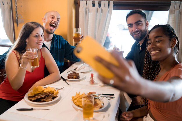 Groep diverse vrienden die een selfie maken met een mobiele telefoon terwijl ze samen genieten van een maaltijd in een restaurant. Vrienden concept.