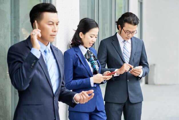 Groep etnische bedrijfsmensen die hun telefoons in openlucht met behulp van