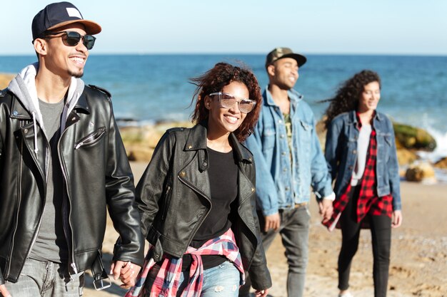 Groep gelukkige Afrikaanse vrienden die in openlucht bij strand lopen.