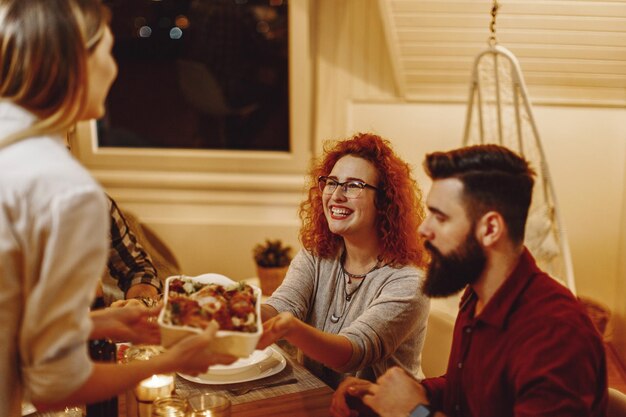 Groep gelukkige jonge mensen die samen dineren aan de eettafel Focus ligt op roodharige vrouw die eten van haar vriend neemt