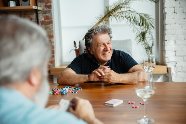 Groep gelukkige rijpe vriendenspeelkaarten en het drinken van wijn