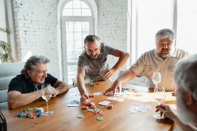 Gratis foto groep gelukkige rijpe vriendenspeelkaarten en het drinken van wijn
