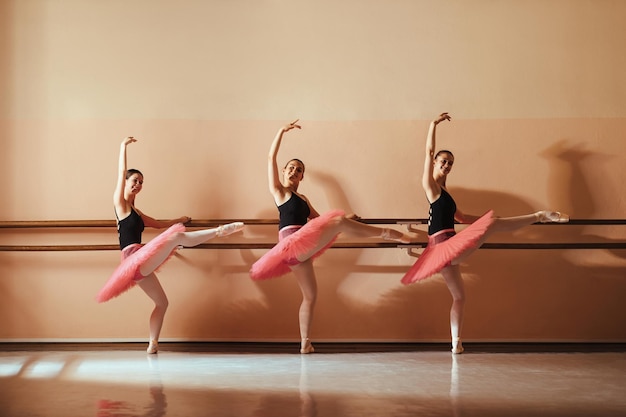 Groep gelukkige tienerballetdansers die een barre vasthouden tijdens het oefenen op de balletschool en naar de camera kijken