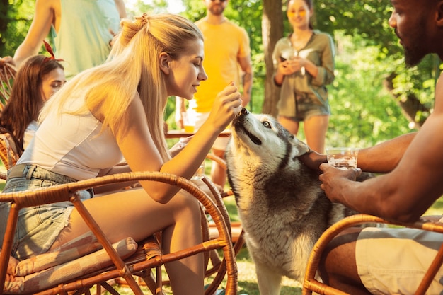 Groep gelukkige vrienden die bier en barbecuepartij hebben op zonnige dag. Samen buiten rusten in een bos open plek of achtertuin. Vieren en ontspannen, lachen. Zomer levensstijl, vriendschap concept.