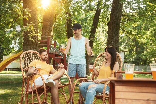 Groep gelukkige vrienden die bier en barbecuepartij hebben op zonnige dag. Samen buiten rusten in een bos open plek of achtertuin