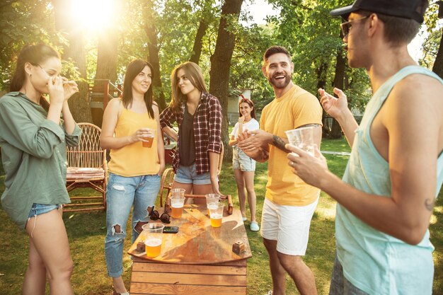 Groep gelukkige vrienden die bier en barbecuepartij hebben op zonnige dag. Samen buiten rusten in een bos open plek of achtertuin