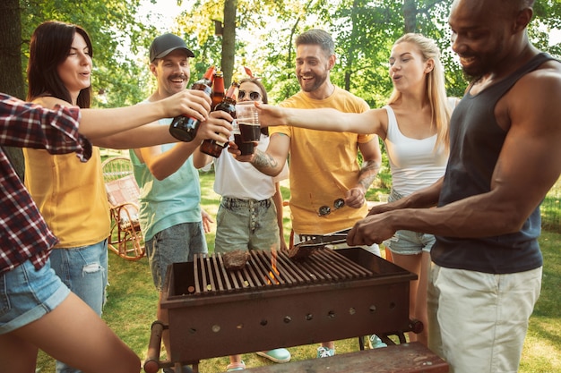 Groep gelukkige vrienden die bier en barbecuepartij hebben op zonnige dag. Samen buiten rusten in een bos open plek of achtertuin