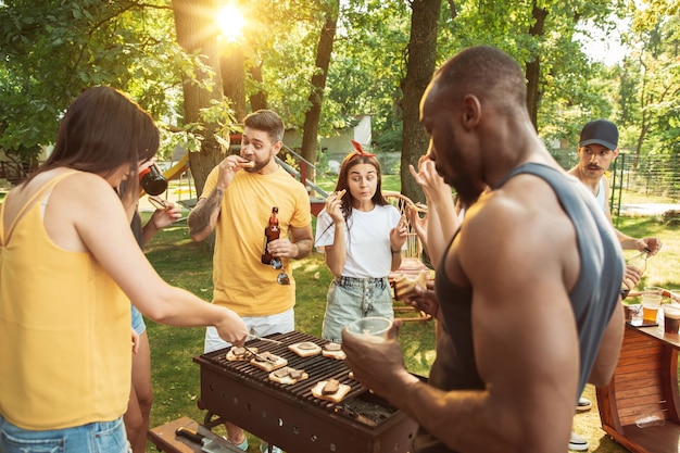 Groep gelukkige vrienden die bier en barbecuepartij hebben op zonnige dag. samen buiten rusten in een bos open plek of achtertuin