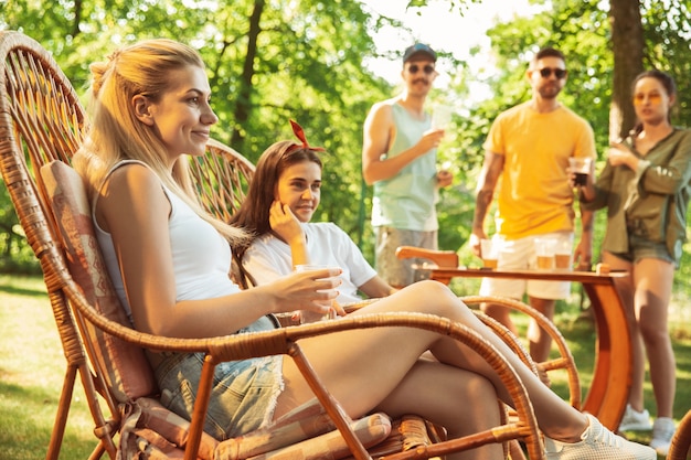 Groep gelukkige vrienden die bier en barbecuepartij hebben op zonnige dag. Samen buiten rusten in een bos open plek of achtertuin