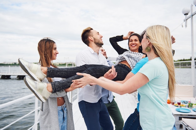 Gratis foto groep gelukkige vrienden op het strand, man die een gelukkige vrouw werpt.