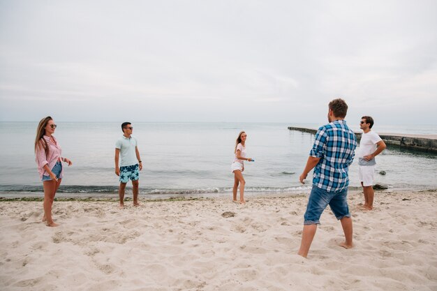 Groep jonge aantrekkelijke vrienden die frisbee op het strand, door het overzees spelen