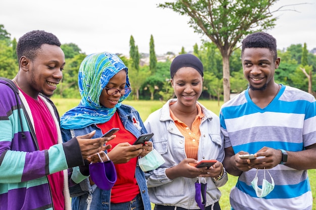 Groep jonge Afrikaanse vrienden met gezichtsmaskers die hun telefoons gebruiken in een park