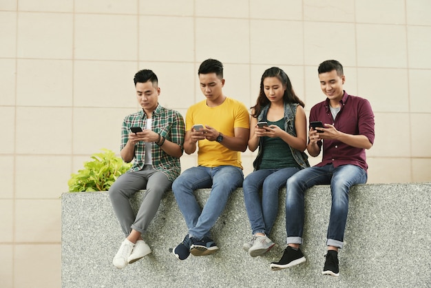 Groep jonge aziatische mensen die in straat zitten en smartphones gebruiken
