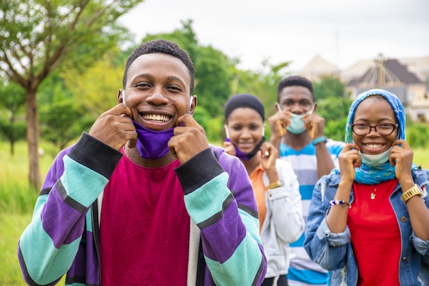 Groep jonge vrolijke Afrikaanse vrienden die gezichtsmaskers dragen en sociaal afstand nemen in een park