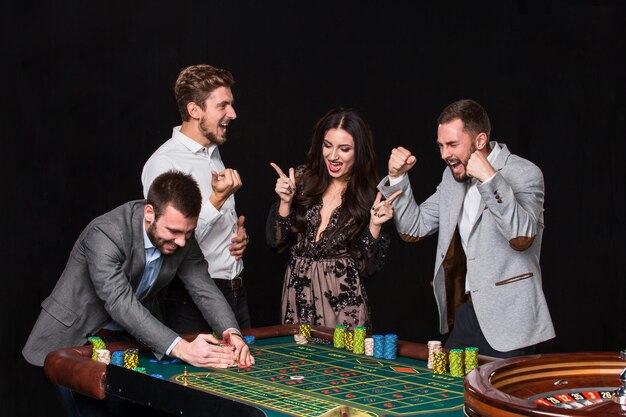 Groep jongeren achter roulettetafel op zwarte achtergrond. De jonge man verheugt zich over de overwinning