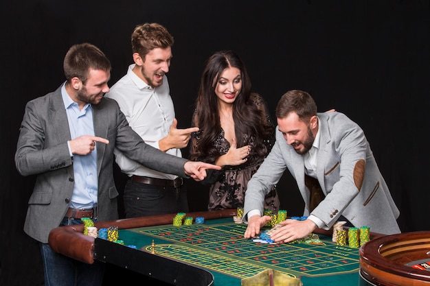 Groep jongeren achter roulettetafel op zwarte achtergrond. De jonge man verheugt zich over de overwinning