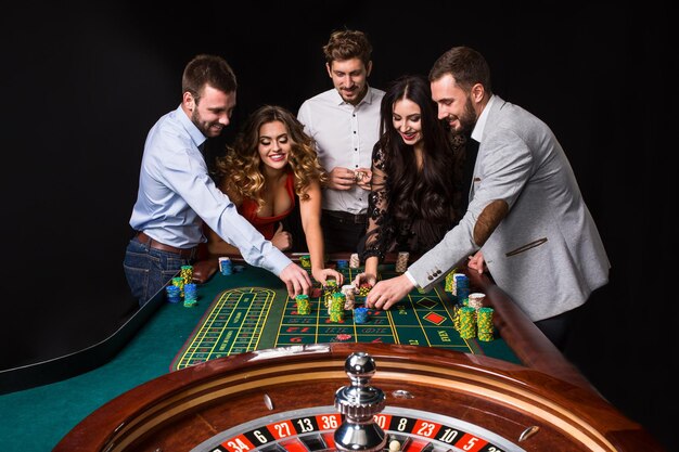 Groep jongeren achter roulettetafel op zwarte achtergrond. Jongeren wedden in het spel