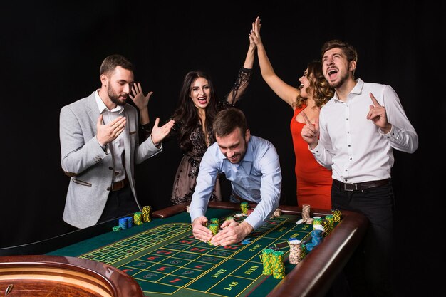 Groep jongeren achter roulettetafel op zwarte achtergrond. Winnende speler. Heldere emoties