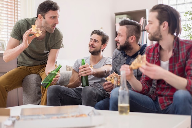 Groep mannen die pizza eten en een biertje drinken
