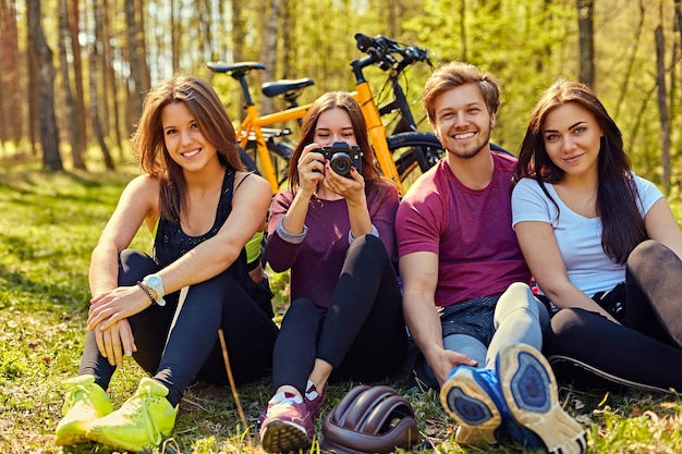 Gratis foto groep mensen ontspannen na fietstocht in een bos. vrouw nemen foto met digitale compacte fotocamera.