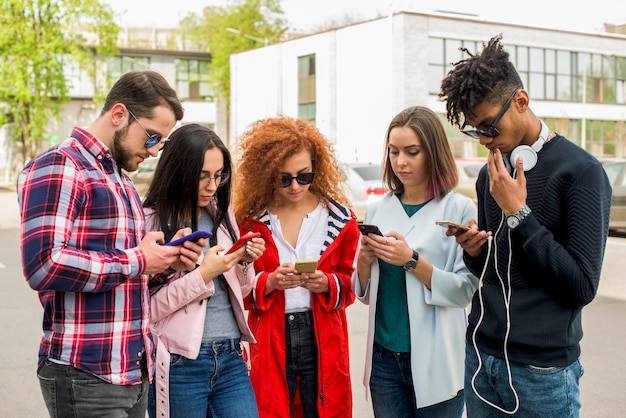 Gratis foto groep moderne vrienden die cellphone gebruiken bij openlucht