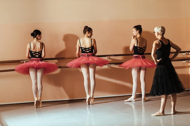 Groep tienerballerina's die en pointe oefenen terwijl ze een les hebben met balletleraar in dansstudio