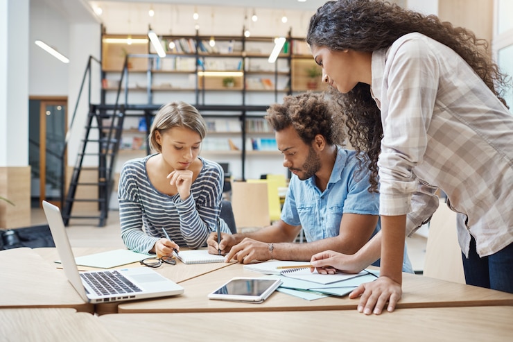 Gratis Foto groep van drie jonge multi-etnische succesvolle zakenmensen zitten in coworking ruimte, praten over nieuw project van concurrent team, plannen maken om hun project te omzeilen.